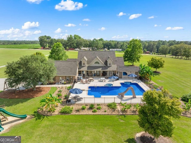 view of swimming pool featuring a lawn, a water slide, a patio area, and a rural view