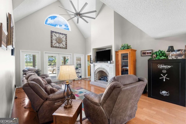 living room featuring light hardwood / wood-style floors, a textured ceiling, a fireplace, high vaulted ceiling, and ceiling fan