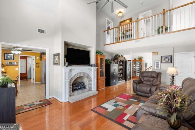 living room featuring a towering ceiling, ceiling fan, wood-type flooring, and a fireplace