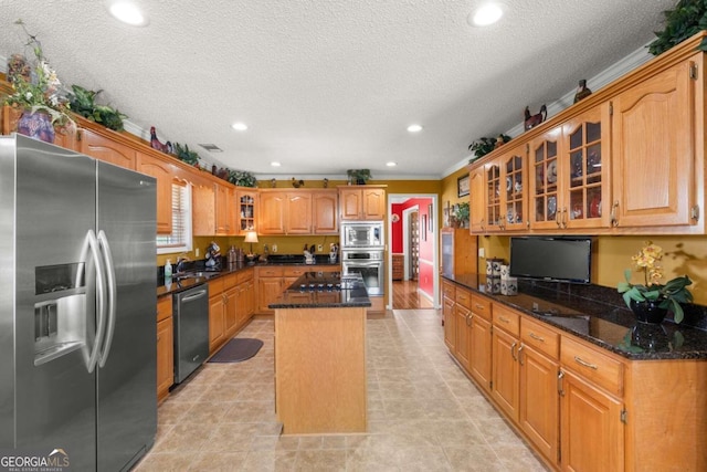 kitchen with dark stone countertops, a center island, a textured ceiling, and appliances with stainless steel finishes