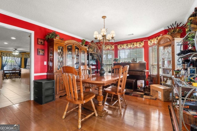 dining space with ornamental molding, a textured ceiling, ceiling fan with notable chandelier, and hardwood / wood-style floors