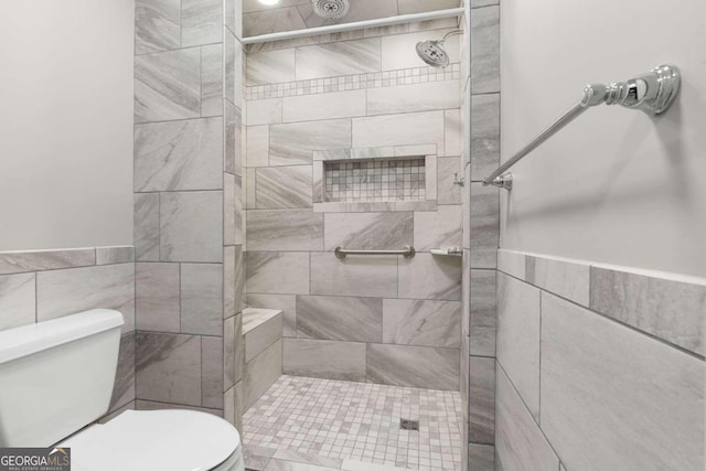 bathroom with a tile shower, tile walls, and toilet