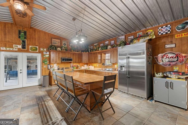 kitchen with pendant lighting, ceiling fan with notable chandelier, wood walls, vaulted ceiling, and appliances with stainless steel finishes