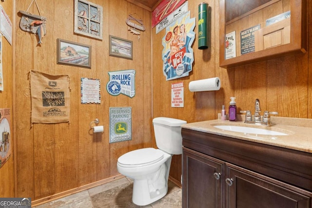 bathroom with tile patterned flooring, wooden walls, toilet, and vanity