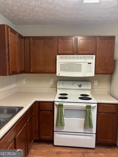 kitchen with white appliances, a textured ceiling, light hardwood / wood-style flooring, and sink