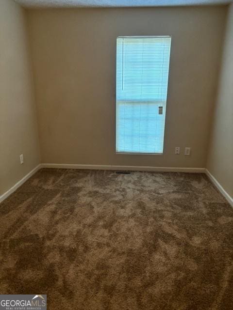 empty room with dark colored carpet and a healthy amount of sunlight