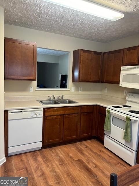 kitchen featuring white appliances, a textured ceiling, sink, and wood-type flooring