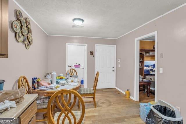 dining space featuring light hardwood / wood-style floors, a textured ceiling, and ornamental molding