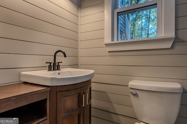 bathroom with vanity, wood walls, and toilet