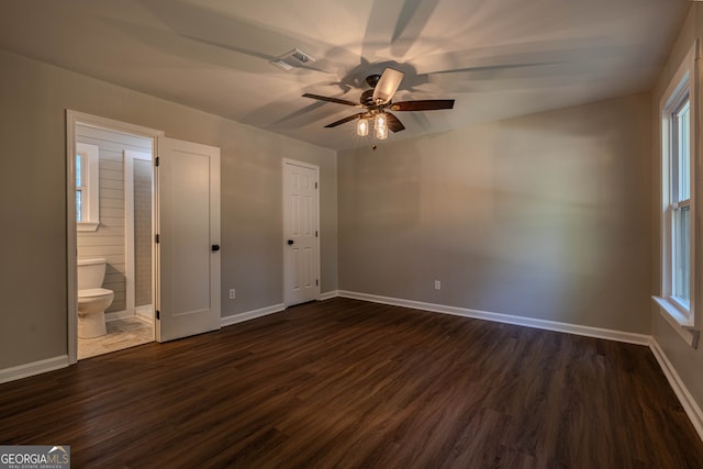 unfurnished bedroom featuring ceiling fan, ensuite bath, and dark wood-type flooring