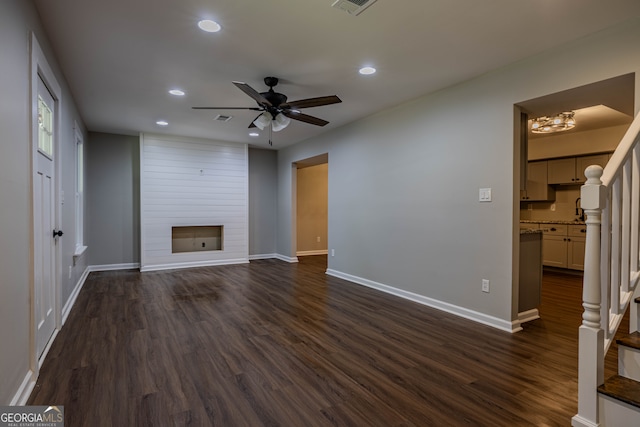 unfurnished living room featuring ceiling fan with notable chandelier, a fireplace, and dark hardwood / wood-style flooring