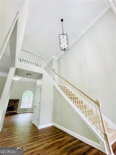 stairway featuring wood finished floors, baseboards, a high ceiling, ornamental molding, and a notable chandelier