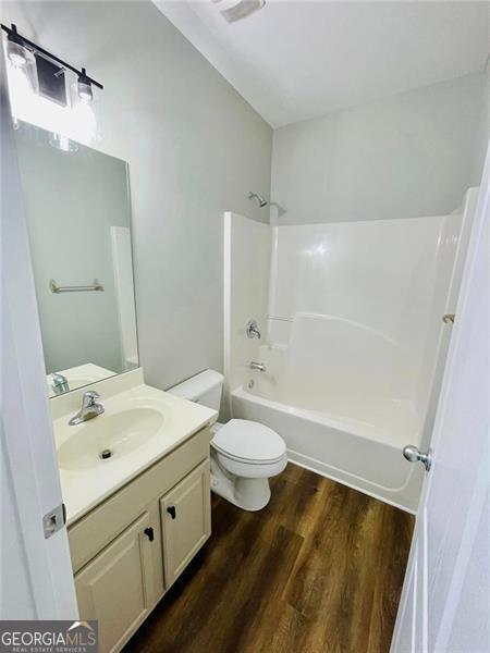 bathroom featuring toilet, vanity,  shower combination, and wood finished floors