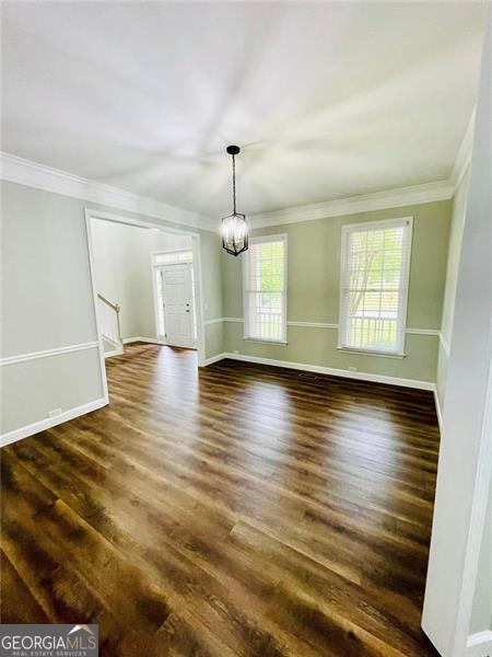 unfurnished dining area with baseboards, stairway, ornamental molding, an inviting chandelier, and dark wood-style floors