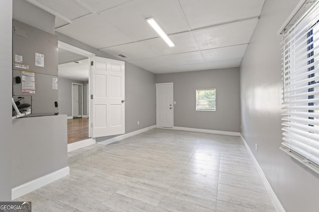 unfurnished room with a drop ceiling, light wood-style flooring, and baseboards