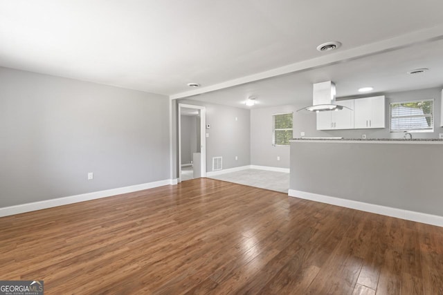 unfurnished living room featuring wood-type flooring, visible vents, and baseboards