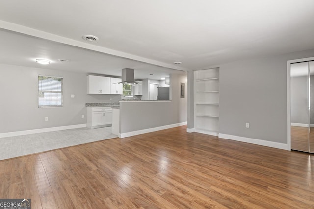 unfurnished living room with light wood-type flooring, built in features, visible vents, and baseboards