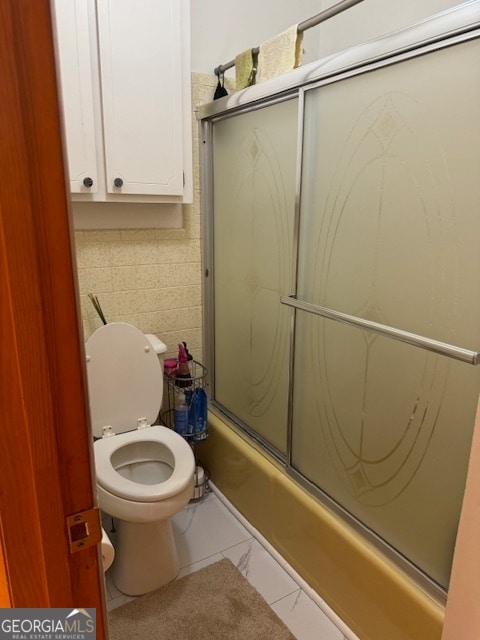 bathroom featuring tasteful backsplash, enclosed tub / shower combo, and toilet