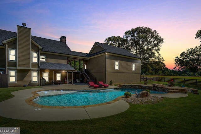 pool at dusk featuring a patio and a lawn