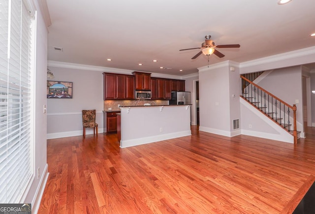 kitchen with open floor plan, appliances with stainless steel finishes, light wood finished floors, and crown molding