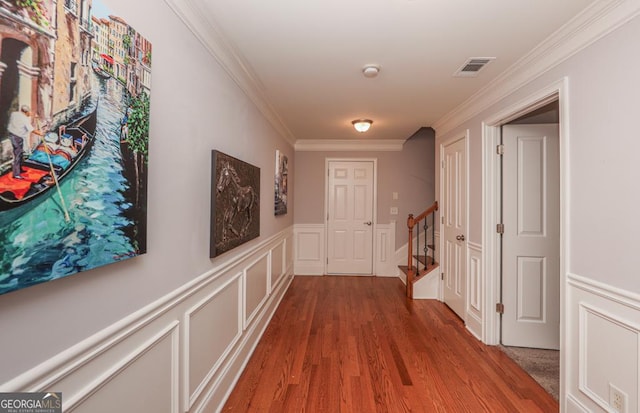 corridor featuring visible vents, a decorative wall, ornamental molding, wood finished floors, and stairs