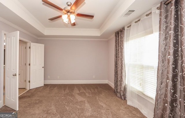 carpeted empty room with baseboards, visible vents, a raised ceiling, and crown molding