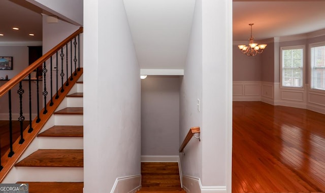 stairway featuring a wainscoted wall, a notable chandelier, wood finished floors, and a decorative wall