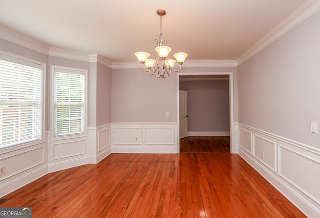 unfurnished dining area with crown molding, a decorative wall, wood finished floors, and a notable chandelier