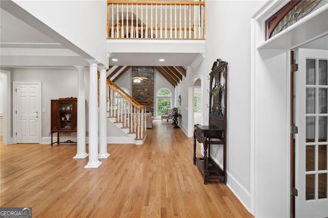 foyer with ornamental molding, light wood-type flooring, ornate columns, and high vaulted ceiling