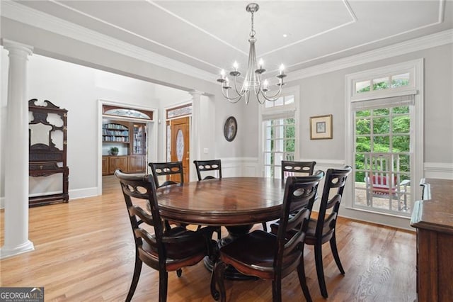 dining area featuring light hardwood / wood-style flooring, a notable chandelier, crown molding, and ornate columns