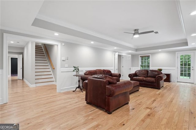 living room featuring light wood-type flooring, crown molding, a tray ceiling, and ceiling fan