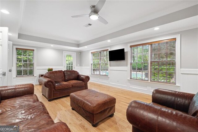 living room with light wood-type flooring, a raised ceiling, ornamental molding, and ceiling fan