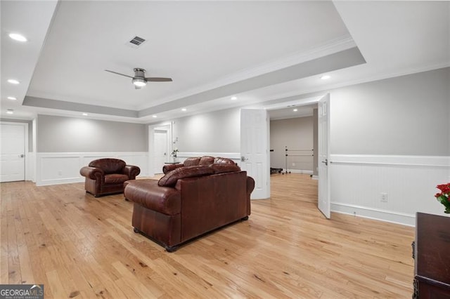 living room featuring light hardwood / wood-style flooring, a tray ceiling, ceiling fan, and ornamental molding