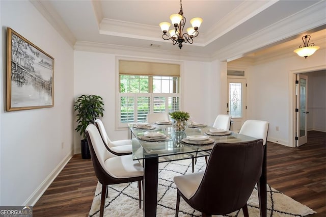 dining area featuring a notable chandelier, crown molding, dark wood-type flooring, and a tray ceiling