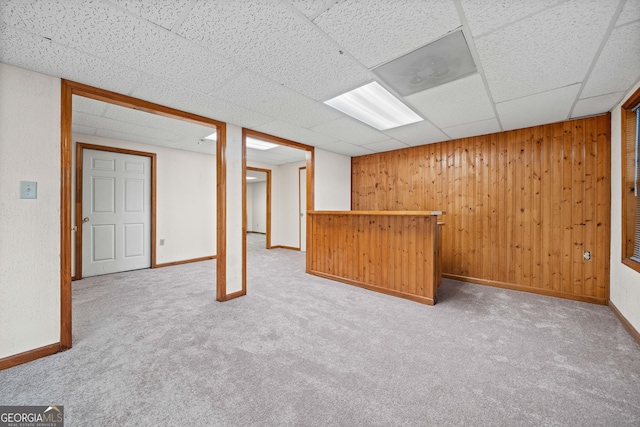 basement with carpet, a drop ceiling, and wooden walls