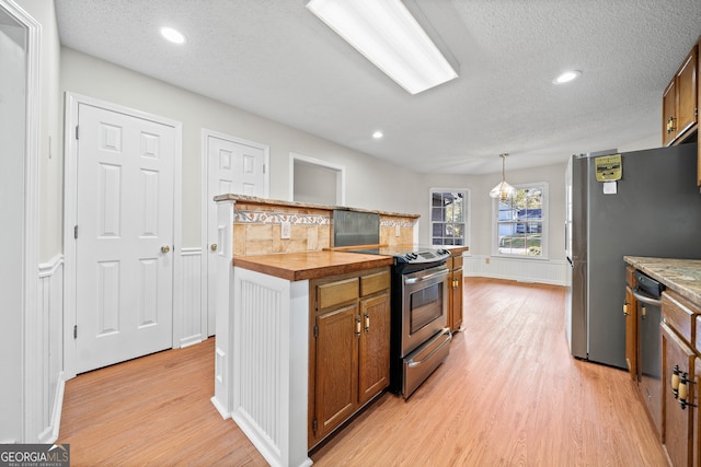 kitchen featuring appliances with stainless steel finishes, wood counters, hanging light fixtures, and light hardwood / wood-style floors