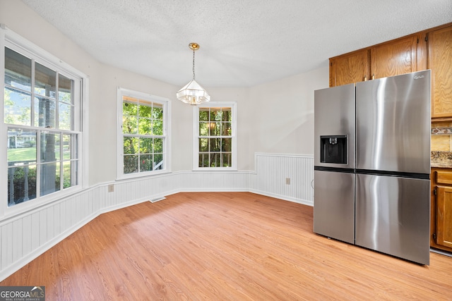 kitchen with a textured ceiling, stainless steel refrigerator with ice dispenser, pendant lighting, and light hardwood / wood-style floors