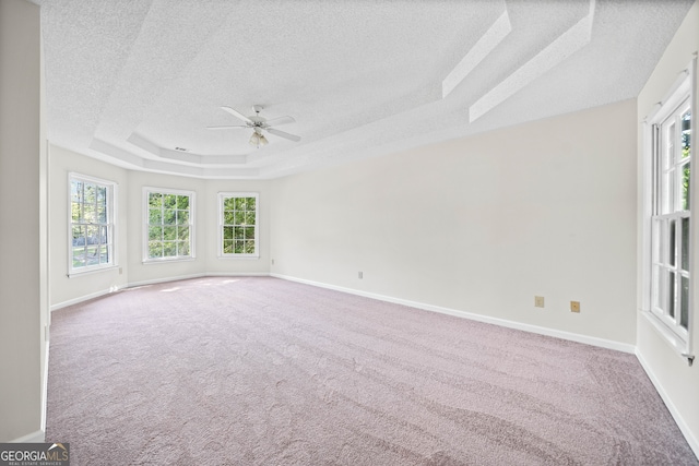 carpeted empty room featuring a textured ceiling, ceiling fan, plenty of natural light, and a raised ceiling