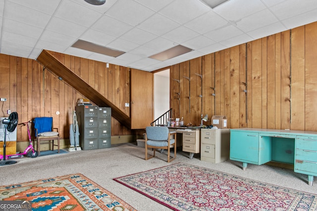 unfurnished office featuring a paneled ceiling, wooden walls, and light carpet