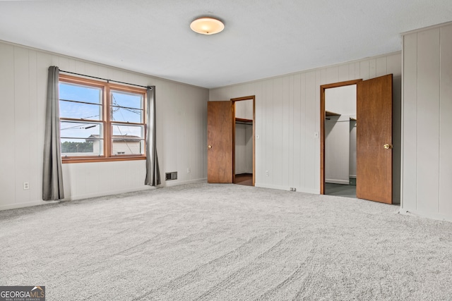 unfurnished bedroom featuring a walk in closet, carpet floors, a closet, and wood walls