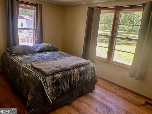 bedroom featuring wood-type flooring, ornamental molding, and multiple windows