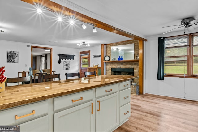 kitchen featuring wooden counters, a fireplace, ceiling fan, white cabinets, and light hardwood / wood-style floors