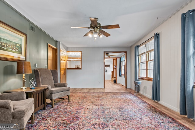 living area with ceiling fan, crown molding, and light hardwood / wood-style flooring