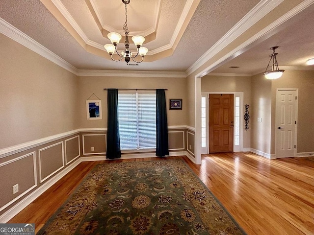 entryway featuring an inviting chandelier, a textured ceiling, ornamental molding, a raised ceiling, and hardwood / wood-style flooring