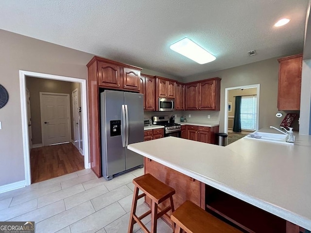 kitchen featuring light tile patterned flooring, sink, a kitchen breakfast bar, kitchen peninsula, and stainless steel appliances