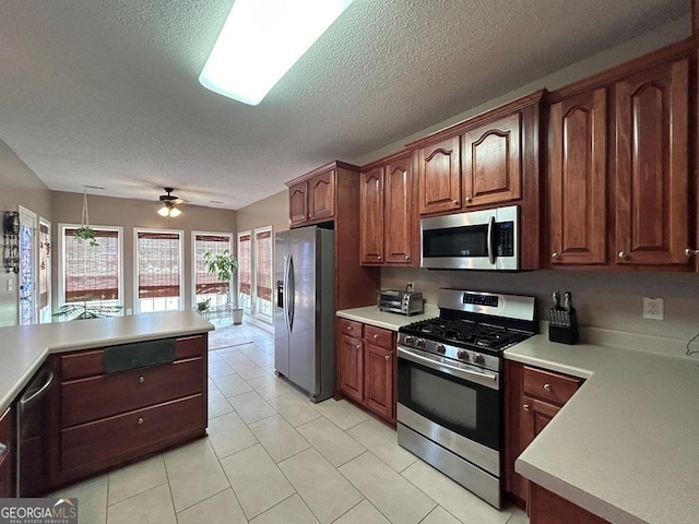 kitchen featuring light tile patterned flooring, decorative light fixtures, ceiling fan, stainless steel appliances, and a textured ceiling