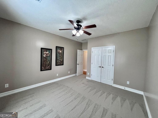 unfurnished bedroom featuring ceiling fan, light colored carpet, a closet, and a textured ceiling