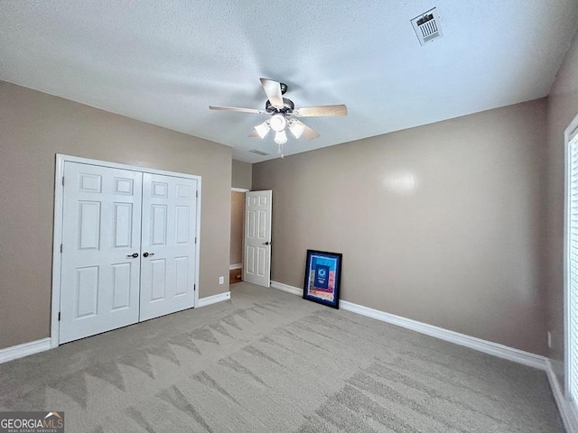 unfurnished bedroom featuring ceiling fan, light carpet, a textured ceiling, and a closet