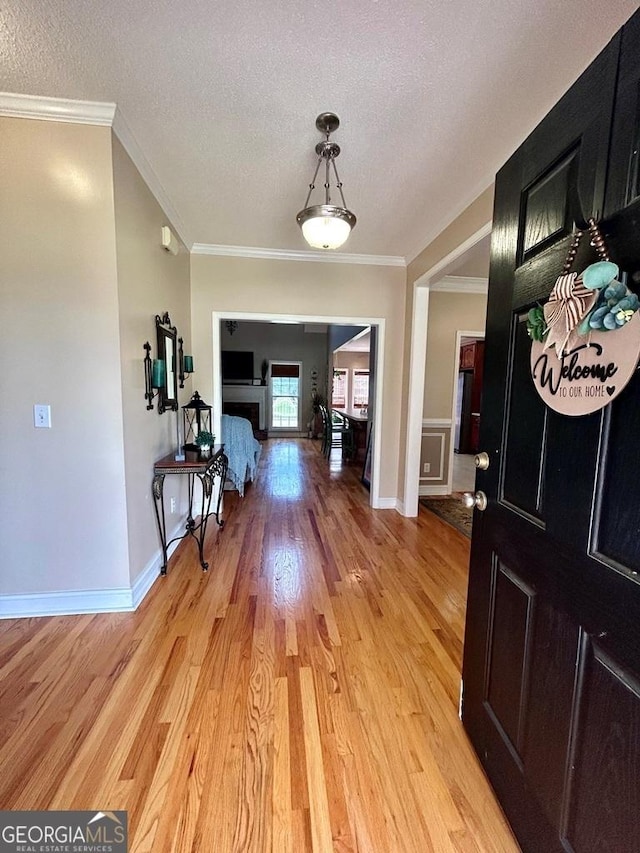 foyer entrance featuring ornamental molding, a textured ceiling, and light wood-type flooring