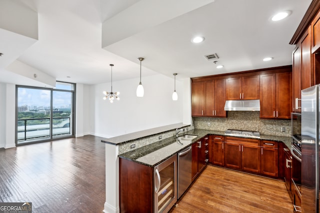 kitchen featuring kitchen peninsula, stainless steel appliances, a notable chandelier, dark stone counters, and light hardwood / wood-style floors